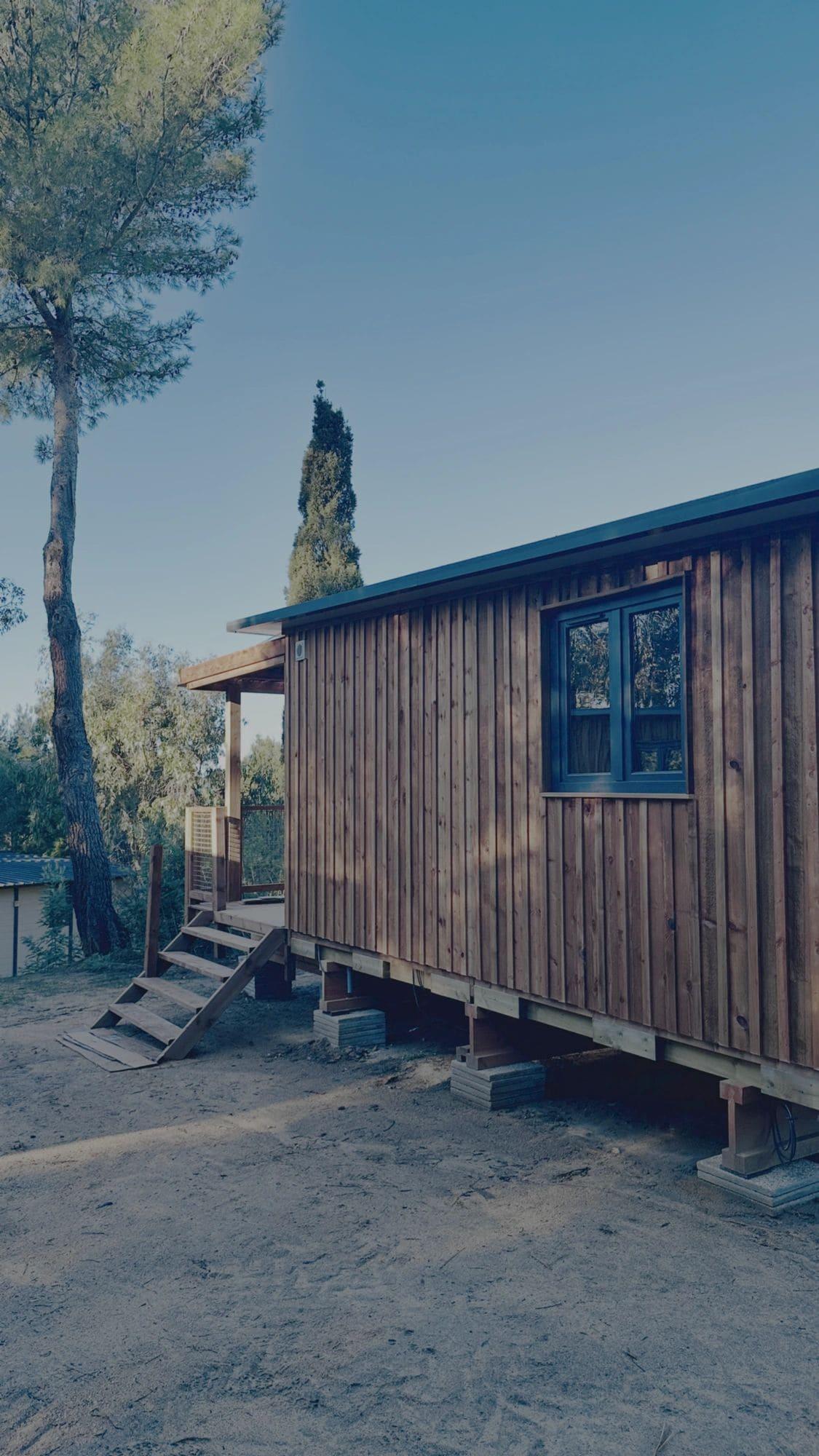 Modern wooden camping cabin in South Corsica with blue roof and tall cypress tree