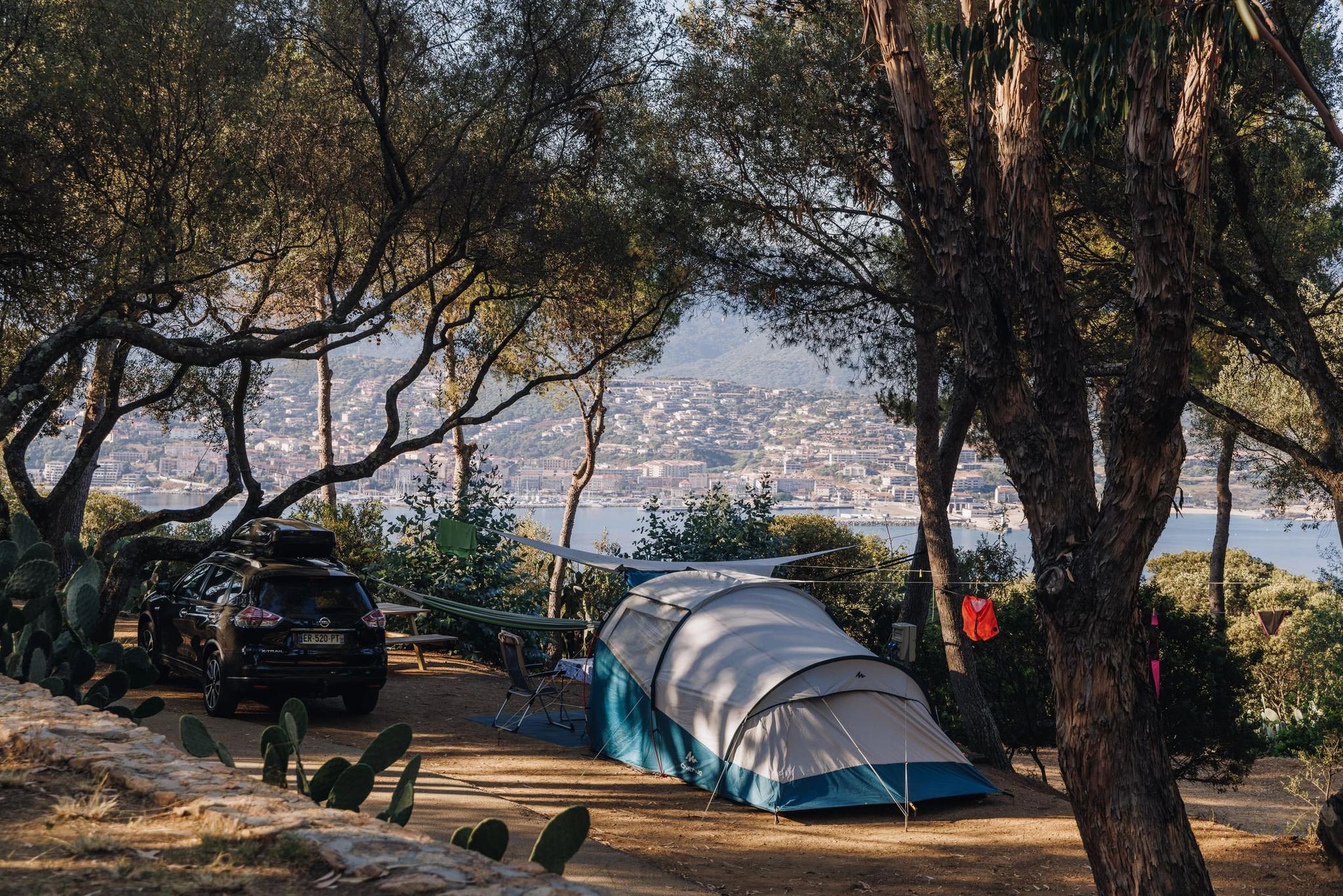Camping in South Corsica with tent and car parked under trees overlooking coastal village