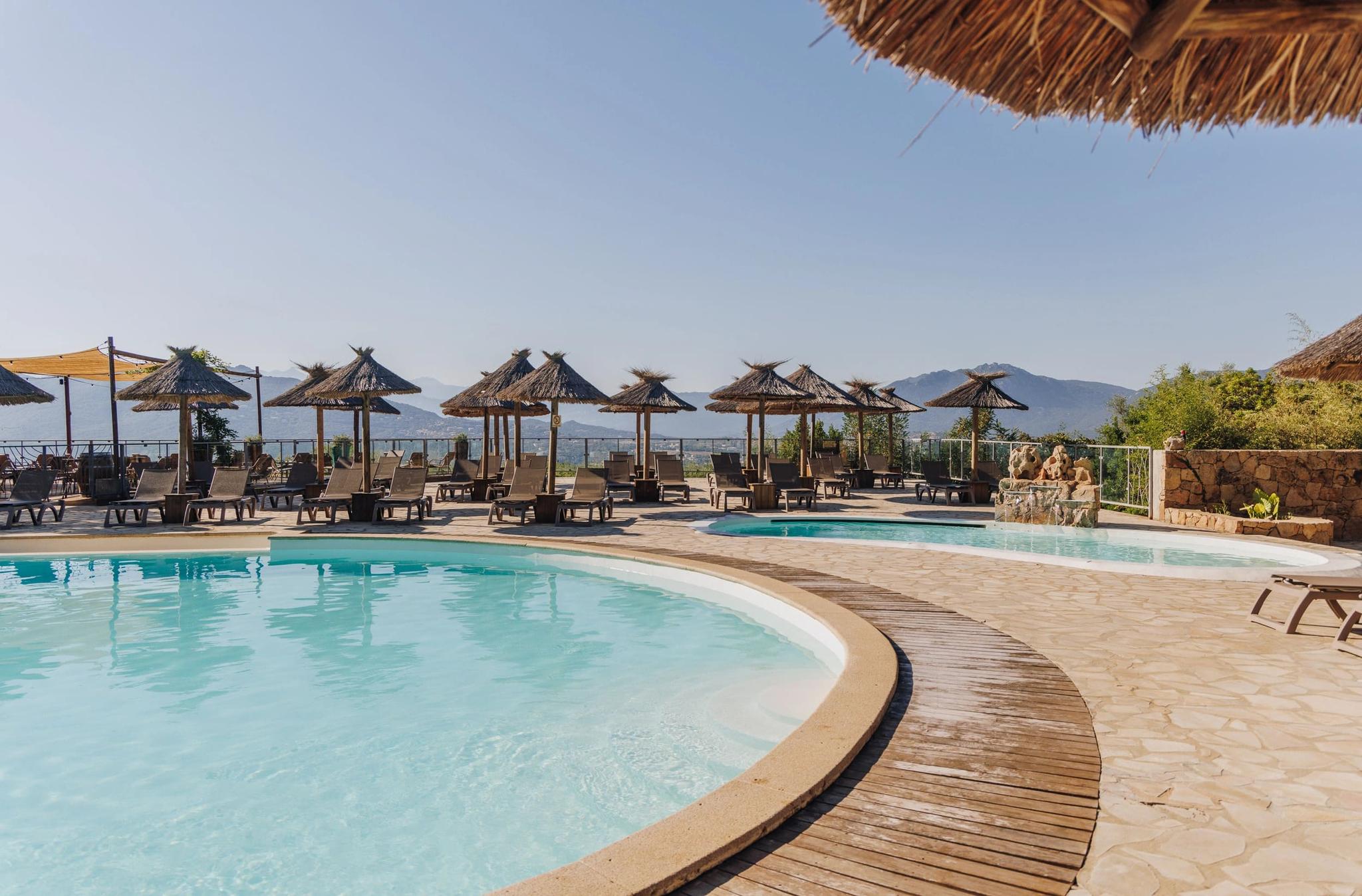 Luxury camping resort pool area with beach umbrellas in South Corsica overlooking mountains